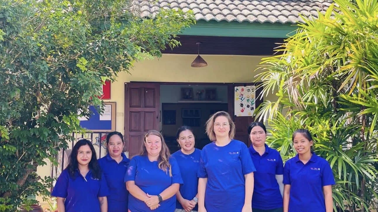 The seven members of the Daisy Chains team in blue school shirts, standing together outside the classroom doorway